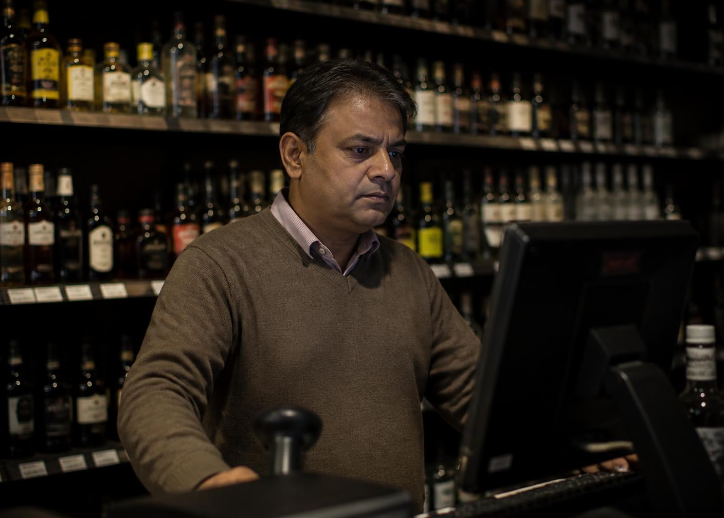 Liquor store owner reviewing NexServe on the counter monitor before opening.